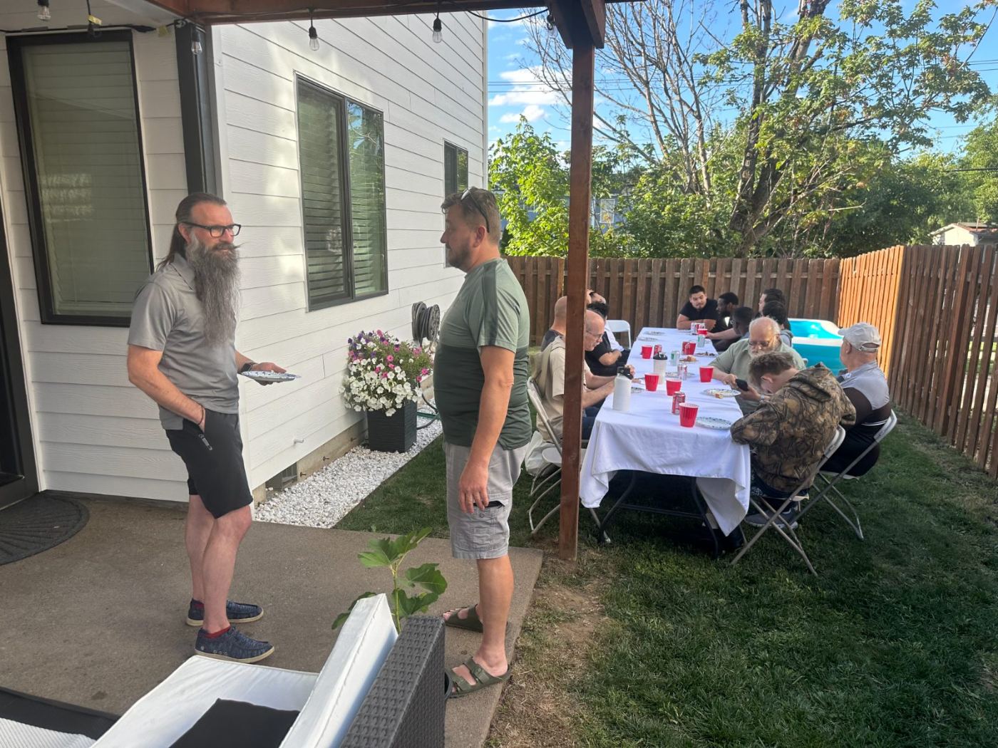 Men gathered in prayer around a long table at a backyard barbecue