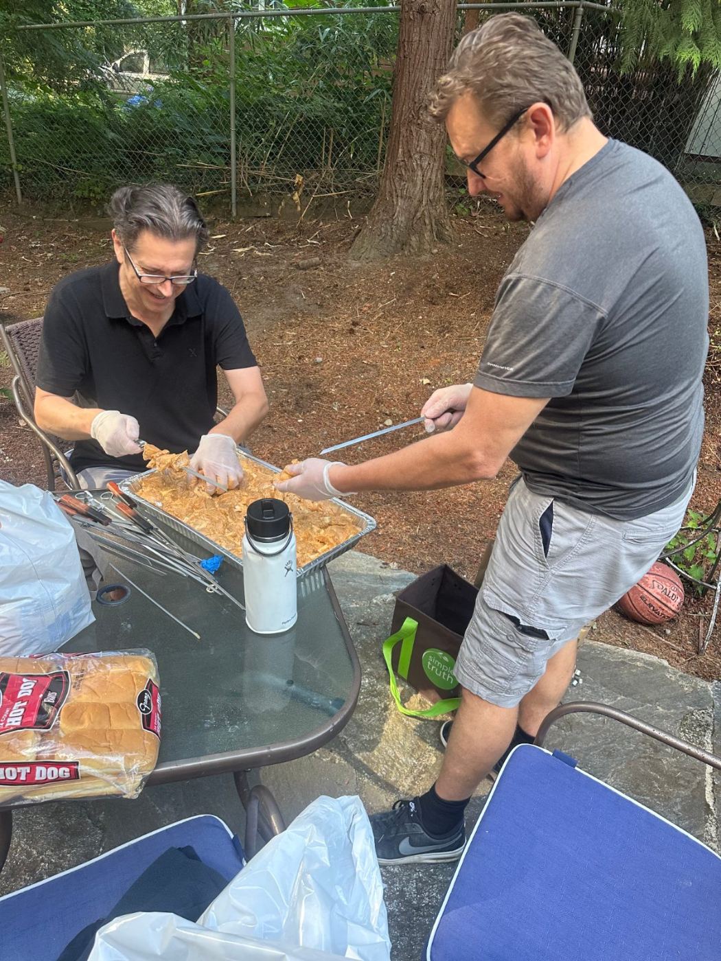 Two men preparing skewers of marinated chicken at a backyard table