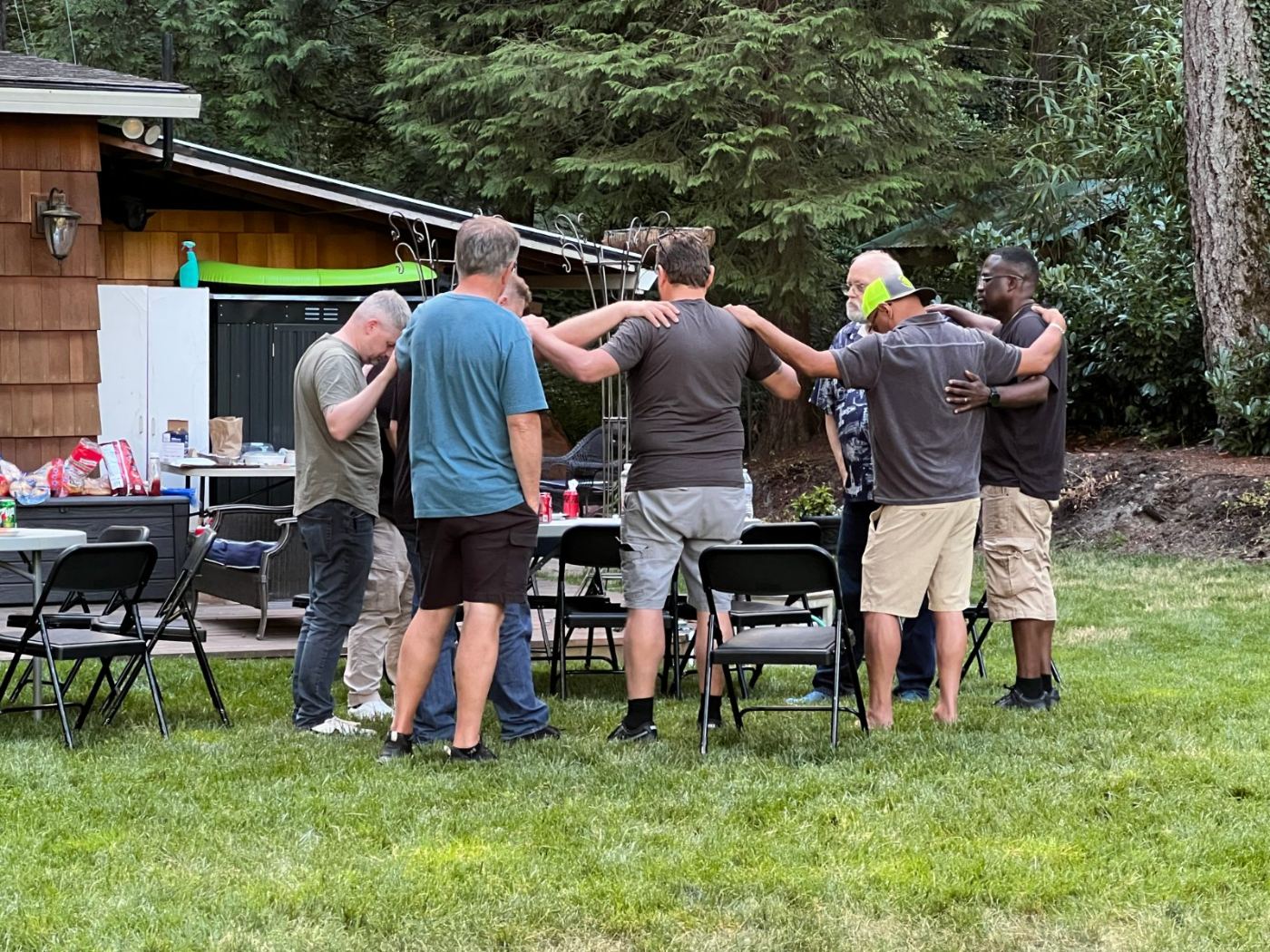 Men gathered in a circle with hands on one another's shoulders, praying together