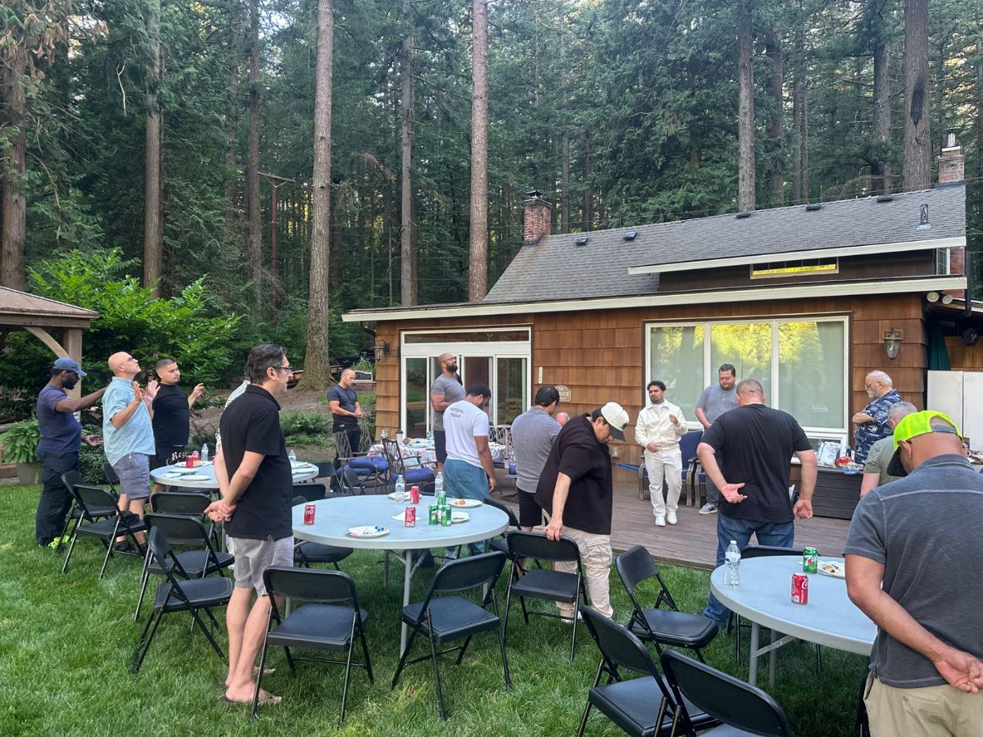 Men worshipping with hands raised beside a cedar cabin