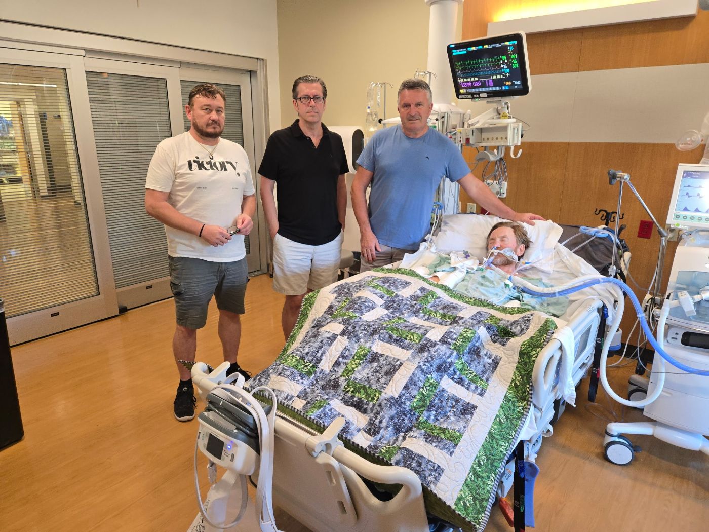 Three men standing in prayer beside a friend's hospital bed
